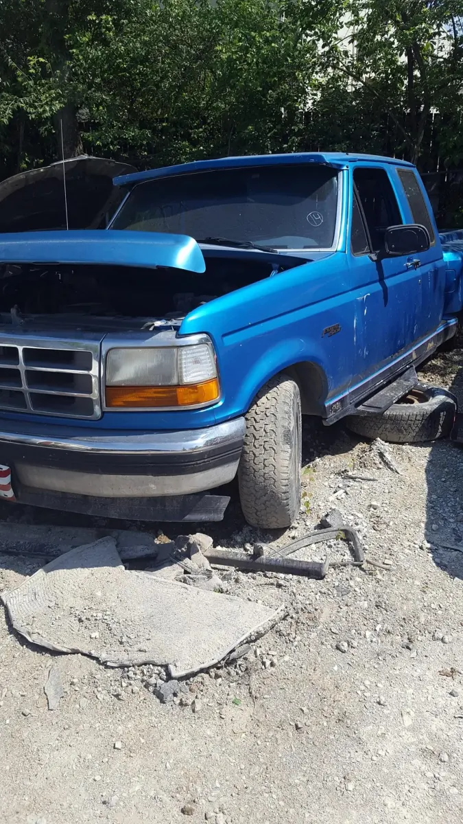 Donor Ford F-150 with its hood up at a full-service salvage yard, engine still in place and ready for inspection