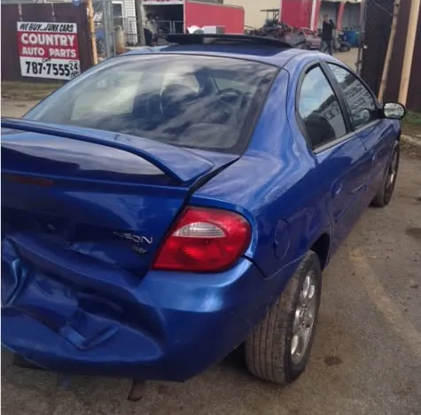 Rear-ended compact car beneath a We Buy Junk Cars sign at an Indianapolis salvage yard